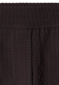 Gros plan sur un tissu noir texturé avec une taille élastique et une couture visible courant verticalement au centre.