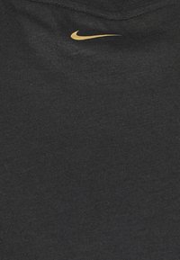 Camiseta de algodón negra con un escote corto y un pequeño logo del swoosh de Nike en dorado en la parte superior izquierda del pecho. Textura suave y lisa.