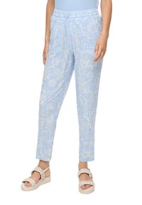 Hellblaue gemusterte Hosen mit einem Kordelzugbund, schmal zulaufenden Beinen und floralen Designs, kombiniert mit klobigen weißen Sandalen.