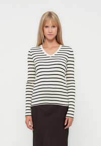 Gestreepte langesleeve trui in crème en zwart, met een V-halsontwerp en een getailleerde pasvorm, gedragen over een effen donkere rok.