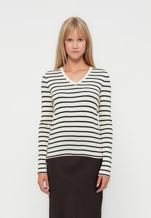 Maglione a maniche lunghe a righe in crema e nero, con scollo a V e forma aderente, indossato sopra una gonna nera a tinta unita.