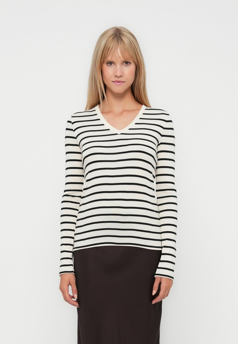 Gestreepte langesleeve trui in crème en zwart, met een V-halsontwerp en een getailleerde pasvorm, gedragen over een effen donkere rok.