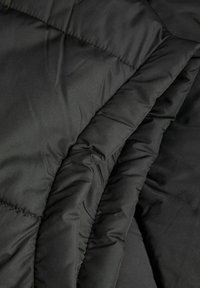 Černá vypolstrovaná tkanina se hladkým povrchem, obsahující prošívané části. Materiál vypadá lehce a izolačně, vhodný pro vrchní oblečení.