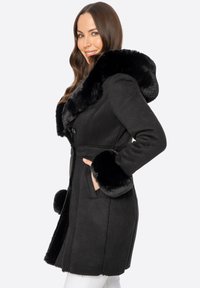 Czarny płaszcz z zamszu z kołnierzem i mankietami z futerka syntetycznego. Posiada dopasowany krój, kieszenie i zapięcie na guziki. Gładka faktura i smukła sylwetka.