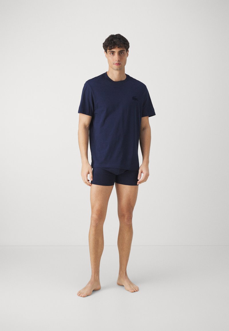T-shirt in cotone blu navy con scollo rotondo e maniche corte, abbinato a boxer dello stesso colore; texture liscia e dettagli di design minimi.