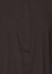 Gros plan sur un tissu brun foncé avec des coutures verticales visibles et une poche partiellement visible sur le côté droit.