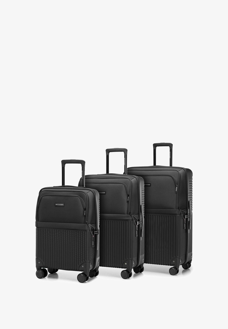 Tre valigie nere con ruote, realizzate in materiale resistente; con superficie testurizzata e dettagli rigati; di diverse dimensioni.