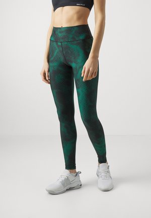 Gröna mönstrade leggings med hög midja, tillverkade av ett stretchigt material med en blandning av mörka och ljusa nyanser, kombinerat med vita träningsskor.