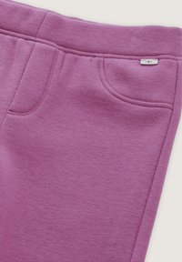 Pantalones de chándal morados hechos de una tela suave, con bolsillos frontales y una pequeña etiqueta de logo. Incluyen costuras visibles y una textura lisa.