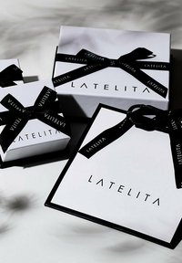 Tre scatole regalo bianche con dettagli neri, con il nome del marchio "LATELITA" in stampa grassetto e legate con nastri neri.