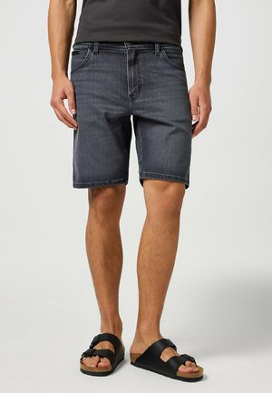 Shorts de mezclilla oscura con corte recto, cinco bolsillos y detalles de costura visibles. Llevados con sandalias negras de tiras ajustables.