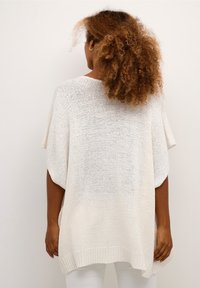 Poncho blanco ligero de punto con mangas cortas, corte holgado y dobladillo acanalado. Presenta una textura de punto abierto para mayor transpirabilidad.