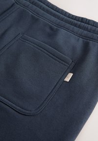Gros plan sur un pantalon de survêtement bleu marine avec une ceinture élastique et une poche arrière rectangulaire avec une petite étiquette en tissu.