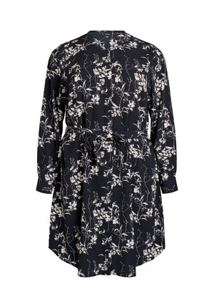 Zwarte jurk met wit bloemenpatroon, lange mouwen, gathered taille en strikdetail. Het materiaal lijkt lichtgewicht en valt soepel.