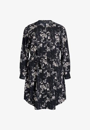 Abito nero con motivo floreale bianco, maniche lunghe, vita arricciata e dettaglio con fiocco. Il materiale sembra leggero e cade morbido.