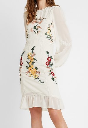 Vestido blanco hasta la rodilla con mangas largas transparentes, bordado floral en amarillo, rojo y rosa, y detalle de volante en el dobladillo.