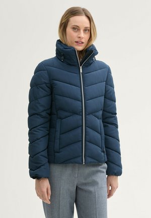 Veste matelassée bleu marine avec un col haut, motif en chevrons, fermeture éclair à l'avant et poignets élastiques. Texture douce et design ajusté.