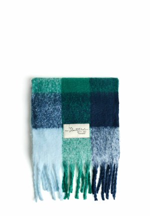Écharpe plissée à carreaux bleus et verts avec des extrémités frangées et une étiquette rectangulaire en tissu blanc cousue au centre.