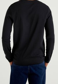 Camisa negra de manga larga hecha de tela suave, con cuello redondo, corte ajustado y dobladillo curvado. Combinada con pantalones de mezclilla azules.