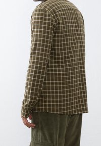 Bruin geruit overhemd met lange mouwen, met witte en blauwe accenten, gemaakt van zachte stof, gecombineerd met olijfgroene ribfluwelen broek.