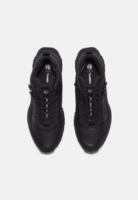 Baskets de sport noires avec une tige en maille texturée, semelle rembourrée et lacets noirs. Présentent un logo sur la languette et des accents réfléchissants.