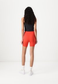 Red athletic shorts with a high waistband, made from stretchy fabric, paired with a black fitted tank top and white sneakers.