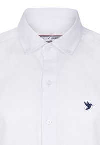 Camisa blanca de botones hecha de algodón, con un collar puntiagudo y un pequeño logotipo de un pájaro azul marino en el lado izquierdo del pecho. Textura suave, diseño clásico.