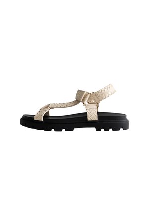 Beige woven sandal with adjustable straps, textured surface, and a thick black sole featuring a lug pattern for traction.