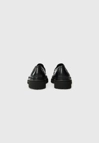 Black leather shoes with a smooth finish, featuring a chunky rubber sole and braided detailing along the heel. Designed with rounded backs.