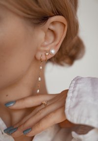 Orecchini d'oro con catene pendenti che presentano piccole perle, accompagnati da un orecchino a perla, su uno sfondo chiaro.