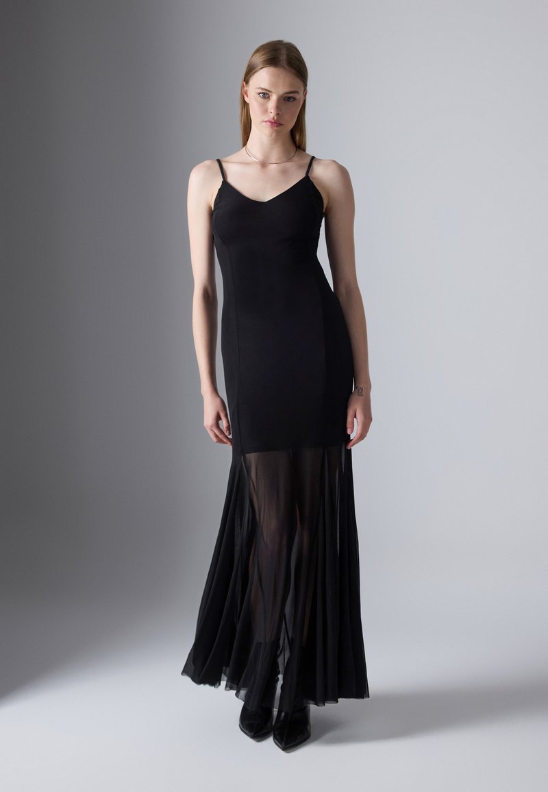 Abito maxi nero con spalline sottili, busto attillato e gonna in chiffon trasparente. Presenta un'orlo a strati con volant e una texture liscia.