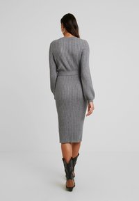 Robe en maille côtelée grise, manches longues, silhouette ajustée, ceinturée à la taille, longueur mi-mollet, assortie à des bottes de cowboy noires.