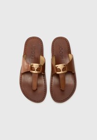 Brune lærsandaler med en tåpost og en gullfarget spenne med dekorativt design. Syddetaljer langs kantene.