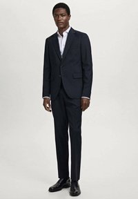 Dark navy suit with slim fit, notch lapels, and two front pockets. Styled with a white dress shirt and black leather shoes.