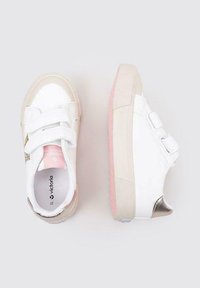 Baskets blanches avec des bandes auto-agrippantes, des accents beiges et une doublure rose pâle. La semelle en caoutchouc texturée présente un motif subtil.