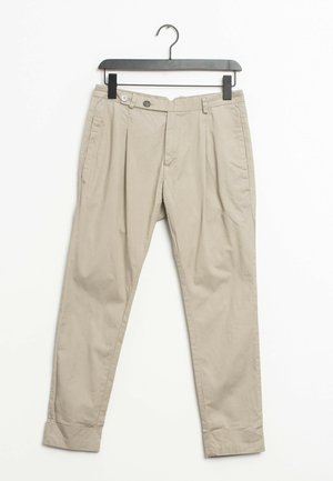 Pantalon beige sur mesure avec ourlets retroussés suspendu à un cintre noir sur fond blanc.