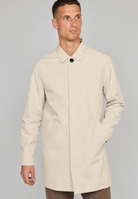 Abrigo impermeable beige de corte recto, con cuello, cierre de botones en la parte delantera y bolsillos laterales. Textura de tela suave y ligera.