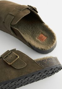Pruunist seemis nahast köndid, mille sees on pehme fliis, reguleeritav pandla ja tekstuuriga must kummitald, millel on täpiline design.