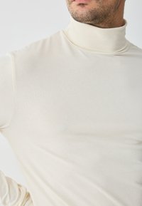 Pulover cu guler înalt, de culoare bej deschis, dintr-un material moale și elastic. Design aderent cu mâneci lungi și guler înalt. Fără modele sau embellishments vizibile.