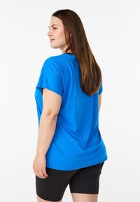 Kurzärmeliges T-Shirt in leuchtendem Blau, hergestellt aus einem glatten, leichten Stoff, kombiniert mit schwarzen Shorts. Verfügt über eine lockere Passform und einen runden Ausschnitt.