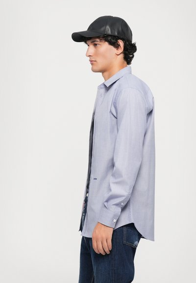 Hellblaues Langarmhemd mit geradem Saum, kombiniert mit einer schwarzen Lederkappe und dunklen Jeans.