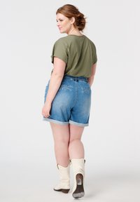 Olijfgroen cropped t-shirt, high-waisted blauwe denim shorts met opgerolde zomen en witte cowboy laarzen, met een relaxte pasvorm en achterzakken.