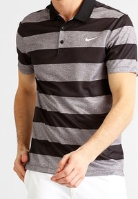 Polo rayé en tissu noir et gris, avec un col, une patte de boutonnage à trois boutons et un petit logo Nike blanc sur la poitrine.