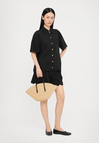 Cămașă neagră cu mâneci bufante, fustă neagră și o geantă din paie texturată. Pantofii negri fără toc completează look-ul.
