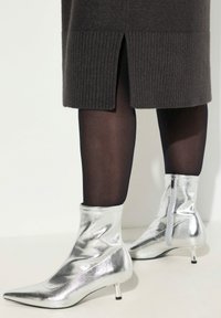 Bottines argentées avec une texture brillante, bout pointu et fermeture éclair sur le côté. Elles présentent un petit talon effilé et un ajustement snug autour de la cheville.