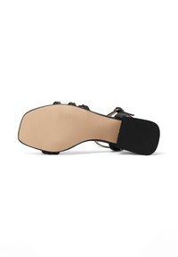 Sandal con tacco nero e design della fascia testurizzata. La suola è beige con dettagli rigati. Il tacco ha una forma a blocco e una finitura liscia.