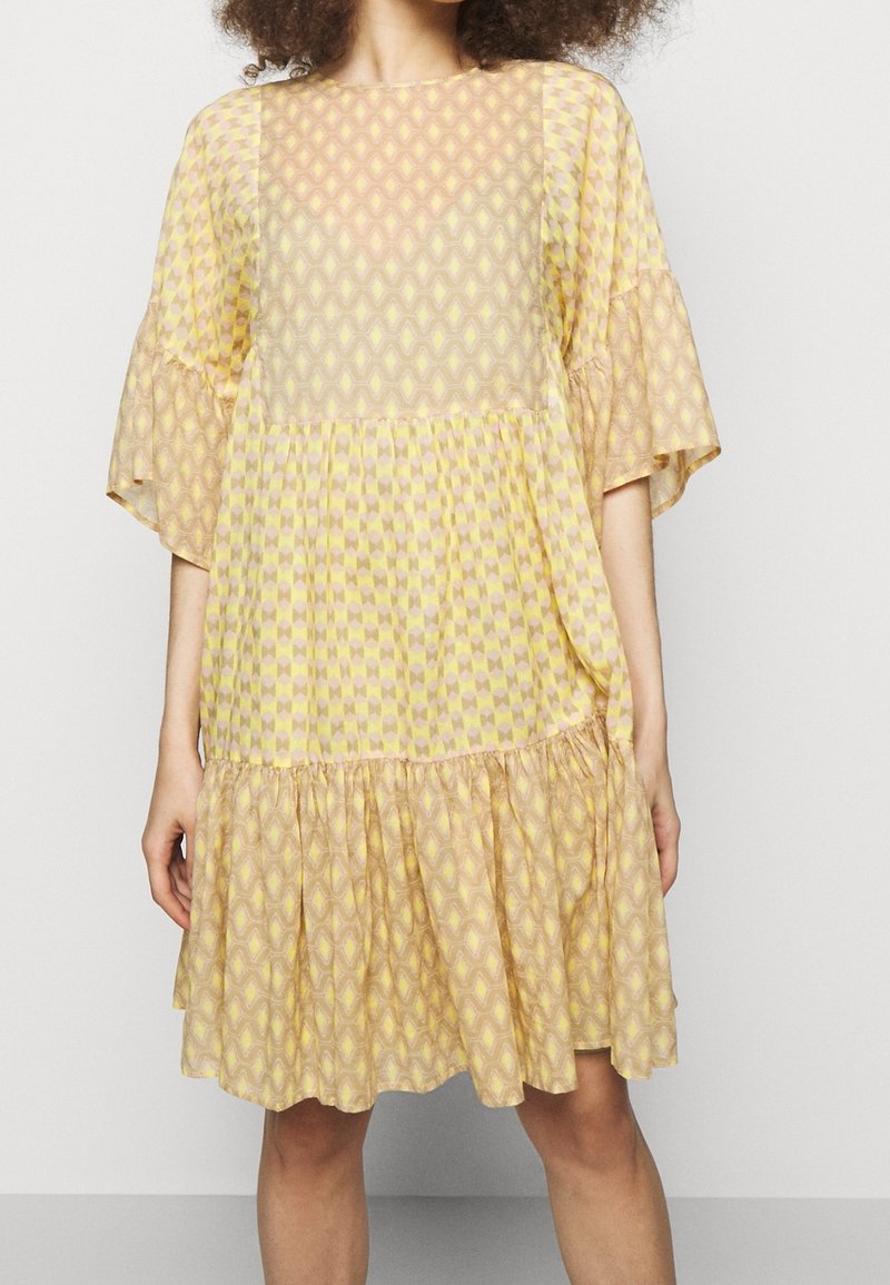 Żółta sukienka w wzory z krótkimi, rozkloszowanymi rękawami i warstwowym, falbaniastym dołem. Materiał zdobiony jest geometrycznymi kształtami w subtelnych odcieniach.