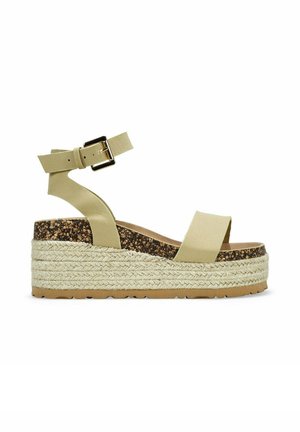 Sandalias de cuña beige con una suela intermedia de corcho, detalles de yute y una correa en el tobillo con una hebilla dorada. Diseño de punta abierta. Suela de goma plana.