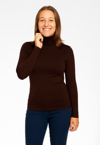 Maglione a maniche lunghe color marrone con colletto alto, realizzato in tessuto elasticizzato, design aderente e texture liscia, abbinato a jeans blu scuro.
