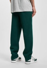 Grønne sweatpants med en afslappet pasform, lavet af blødt stof. Har et enkelt design og er parret med hvide og grønne sneakers.